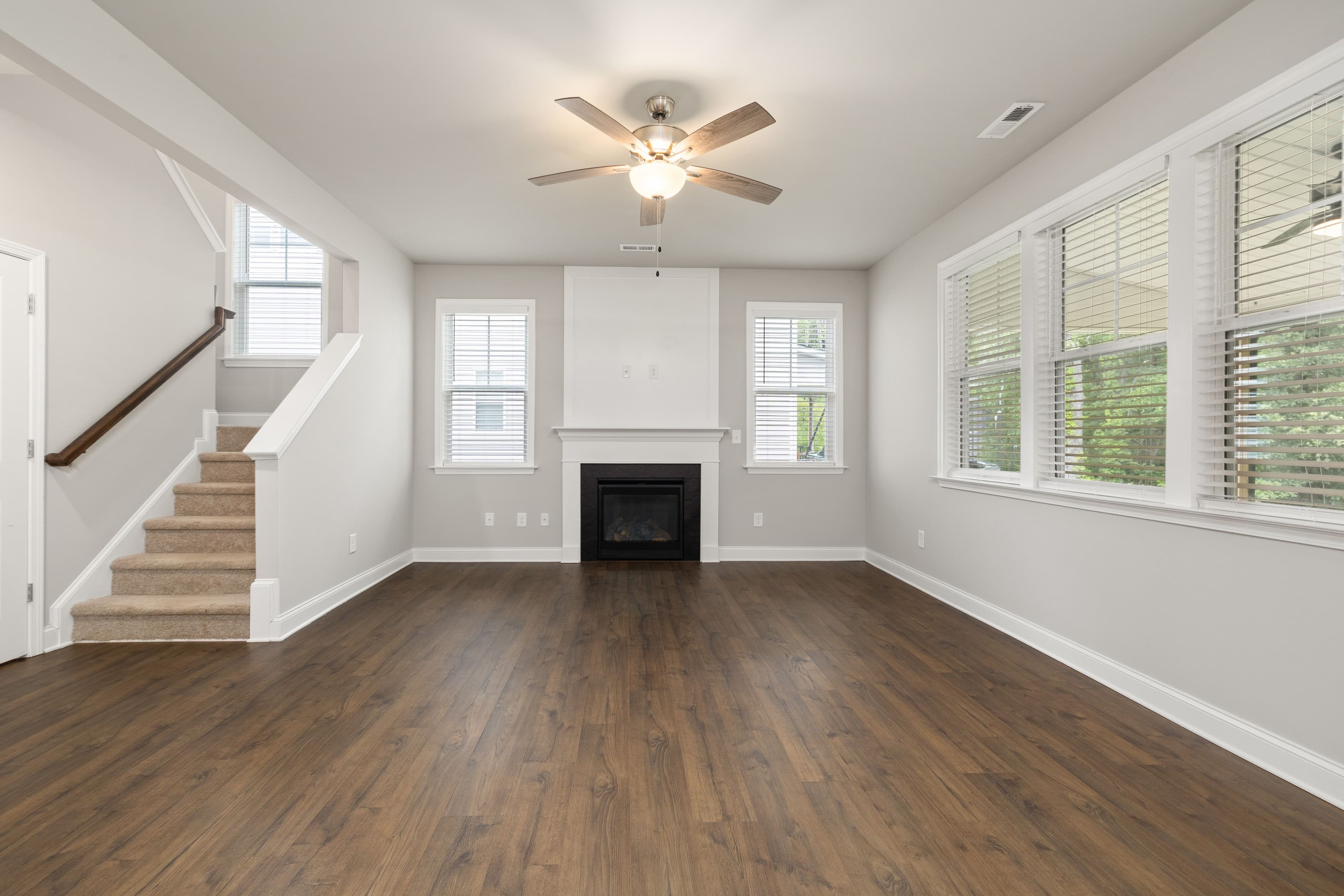 The living room before staging — an empty room with a fireplace, staircase, and large windows